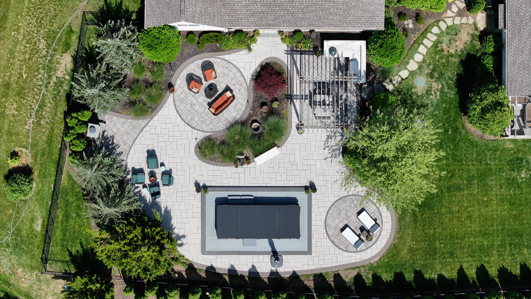 Top-down drone view of custom paver patio layout with circular lounges, pergola dining pad, hot tub surround, and curved landscape beds, Tennessee