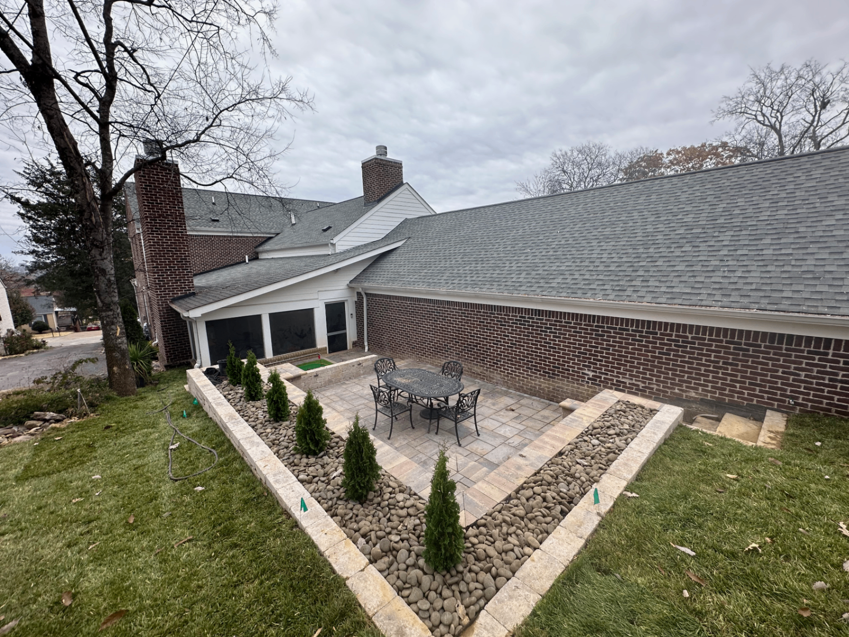 Side courtyard paver patio with cast aluminum dining set, raised stone planter walls, river-rock borders, and screened porch, Tennessee