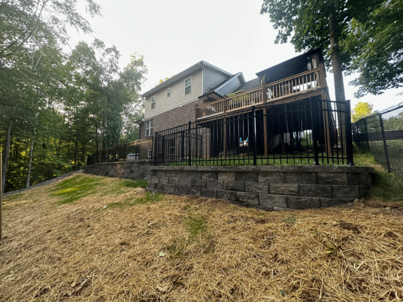 Long engineered retaining wall below black metal fence on sloped backyard property, Tennessee