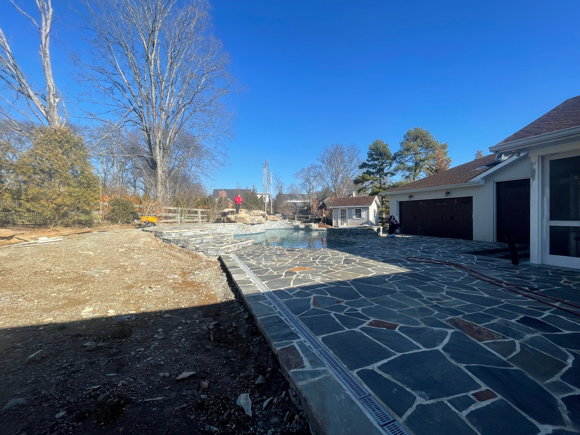 Irregular flagstone patio surrounding a newly built pool with stacked stone retaining walls and waterfall feature beside a white home, Tennessee