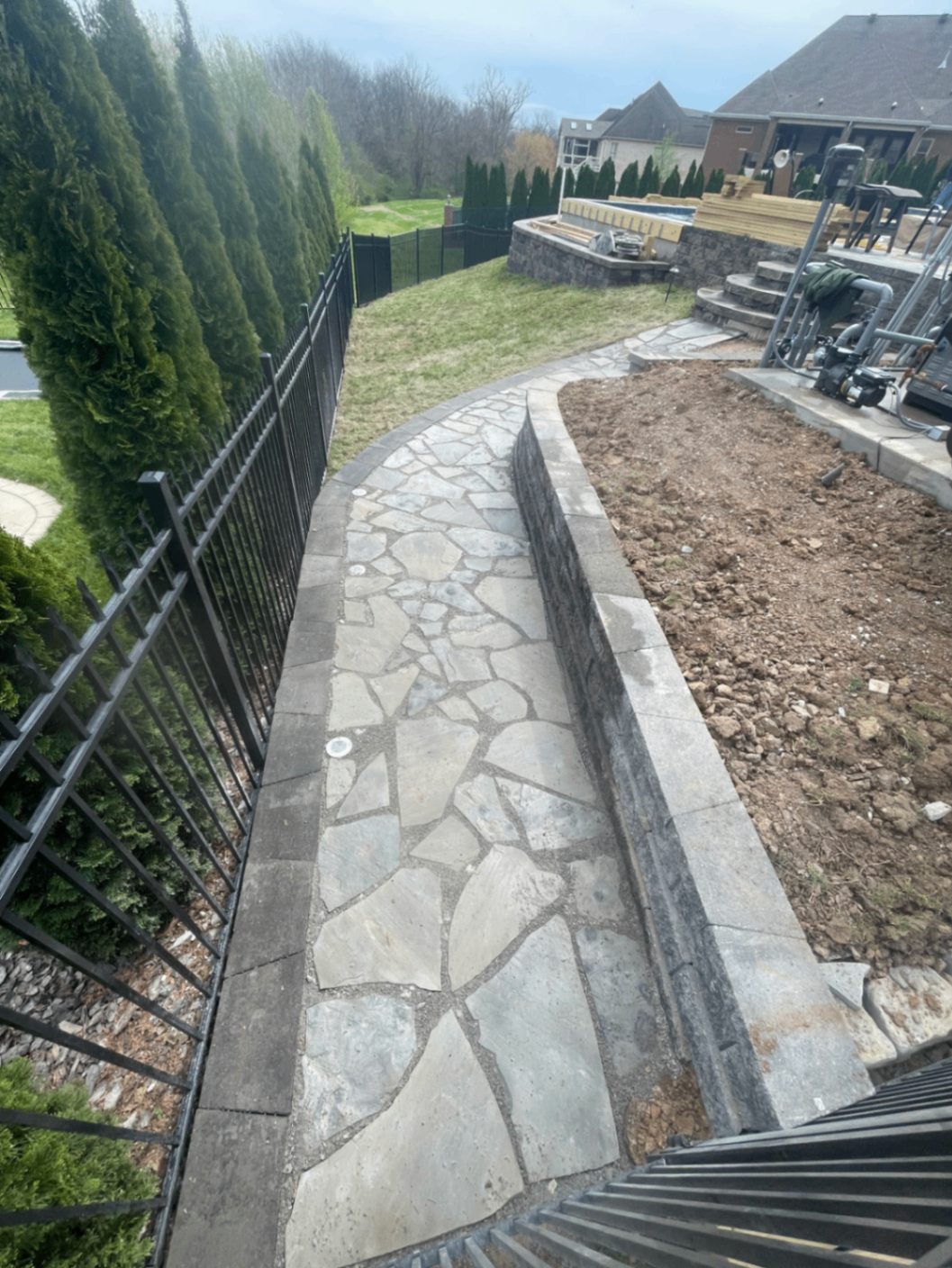 Curved flagstone walkway with paver border running along iron fence toward pool deck, Tennessee