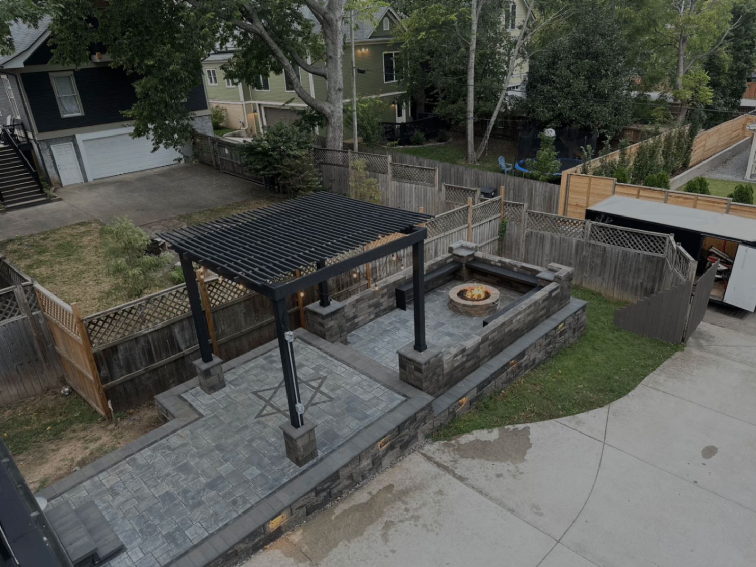 Aerial view of full backyard transformation with black steel pergola, paver patio, fire pit, and tiered seat walls, Nashville TN