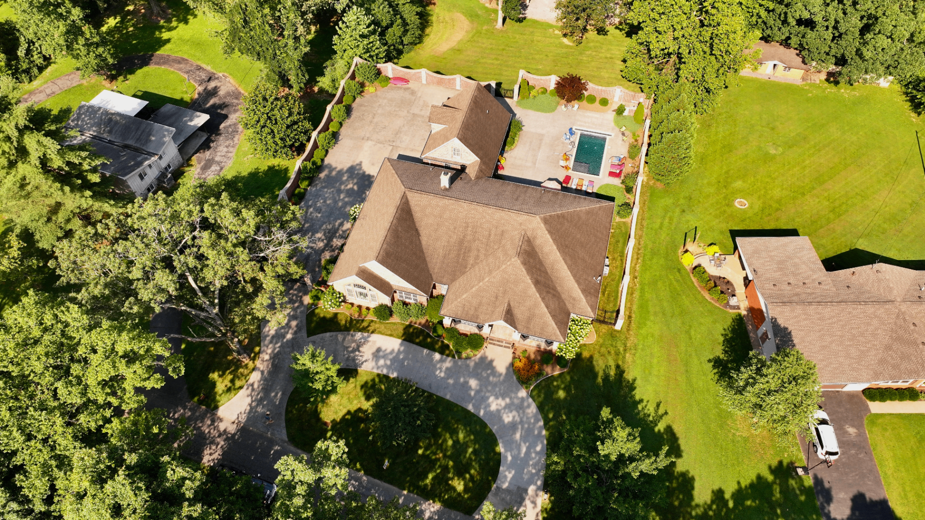 High aerial view of estate property with curved drive, expansive pool courtyard, brick privacy walls, and surrounding lawns in Tennessee