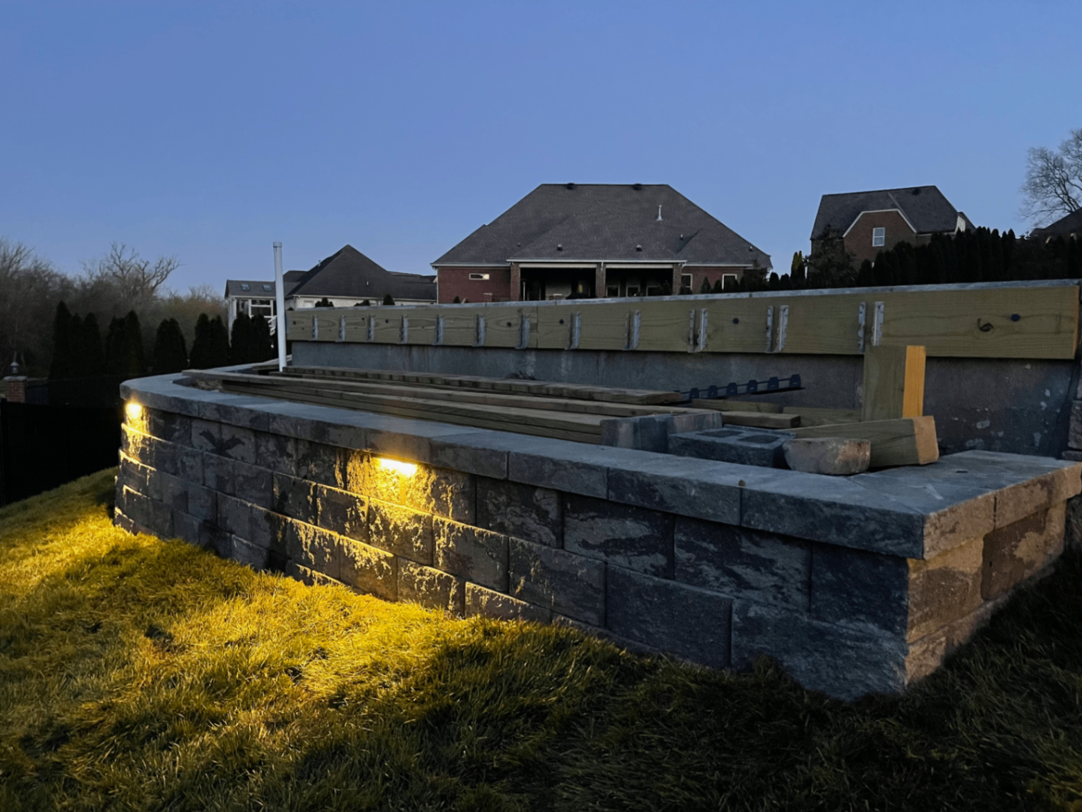 Poolside retaining wall under construction with integrated wall lighting at dusk, Tennessee
