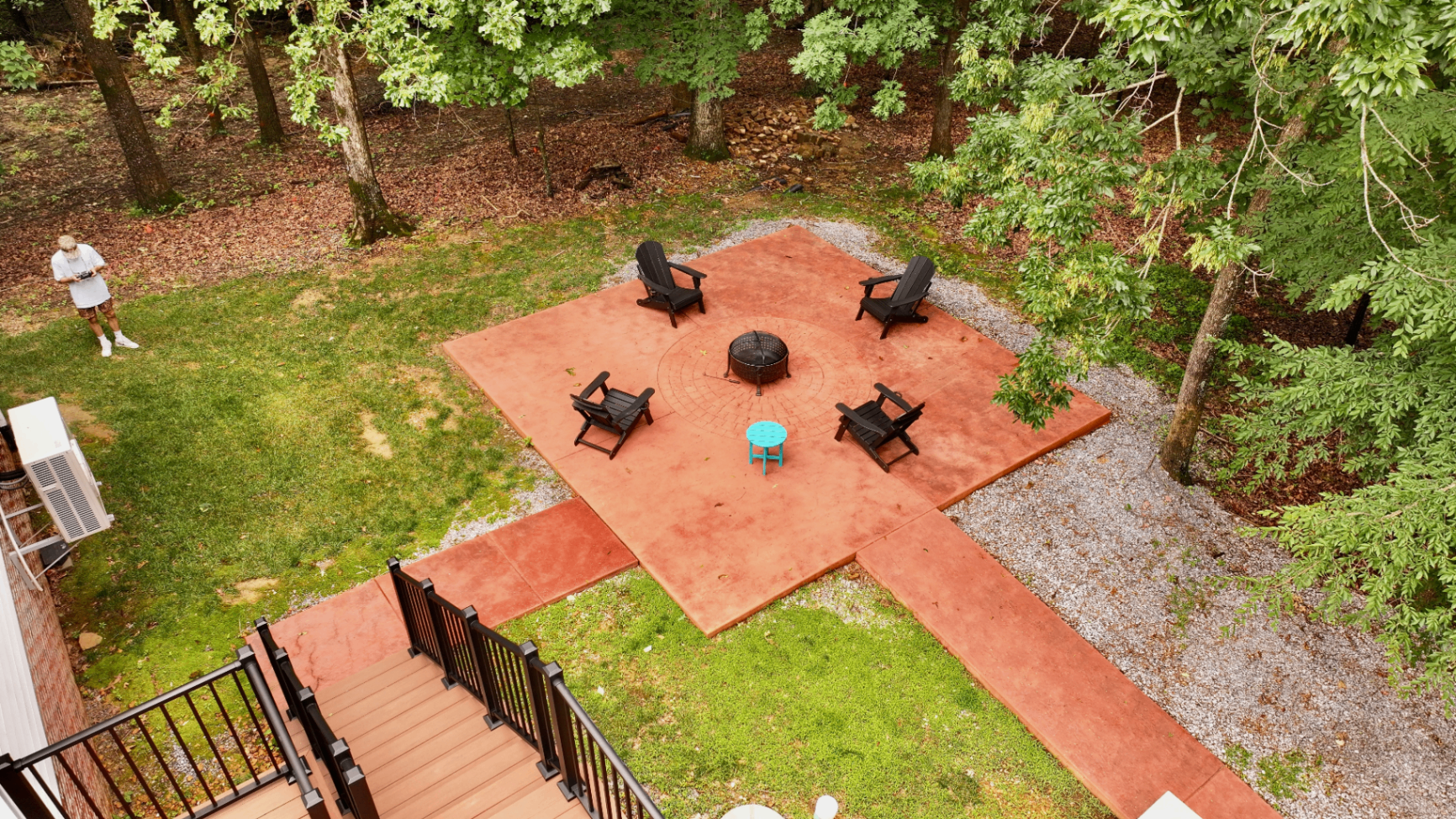 Aerial view of stained terracotta concrete patio with central fire pit and Adirondack chairs in wooded backyard, Tennessee